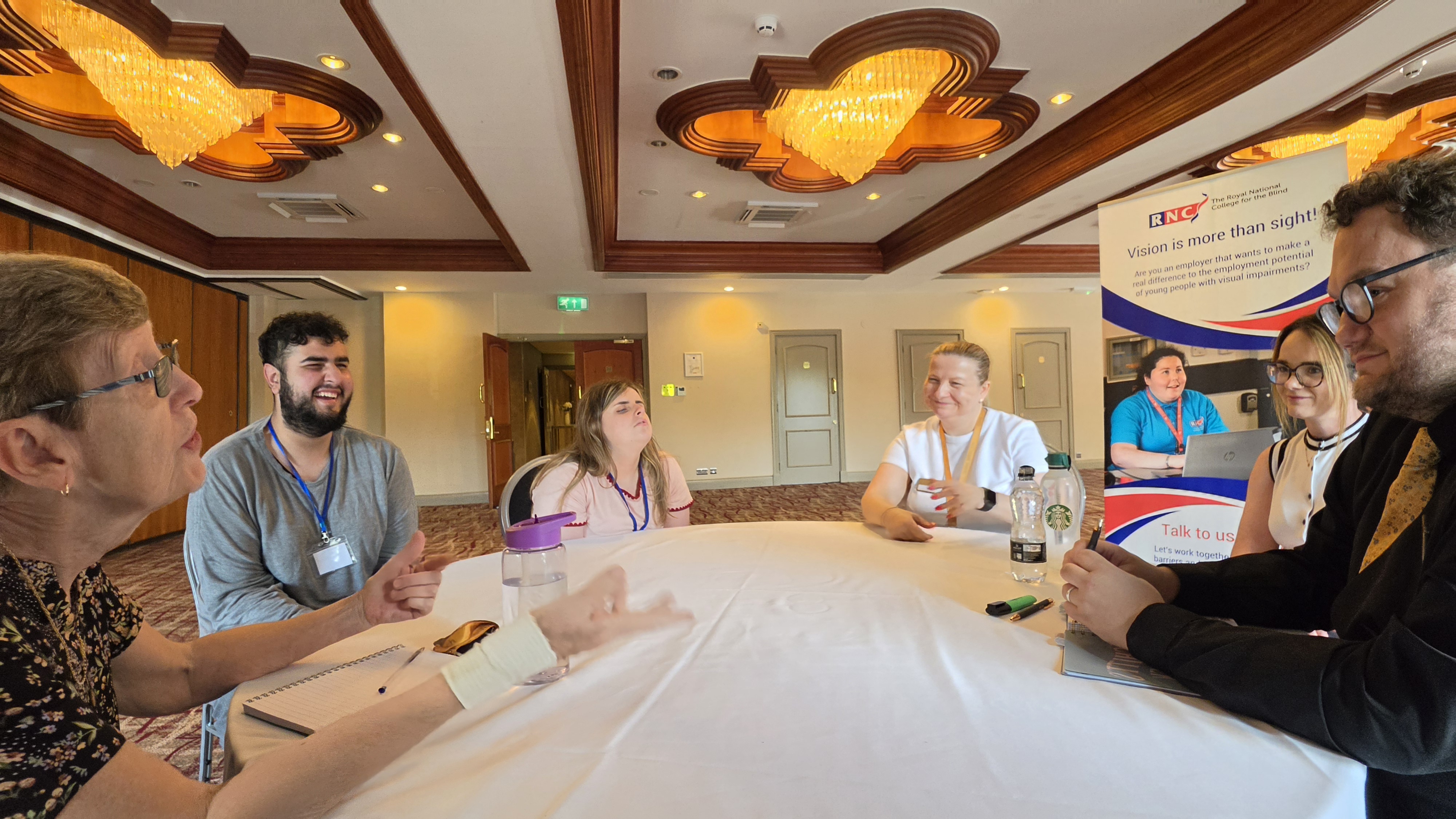 a group of people sitting at a circular table chatting and smiling