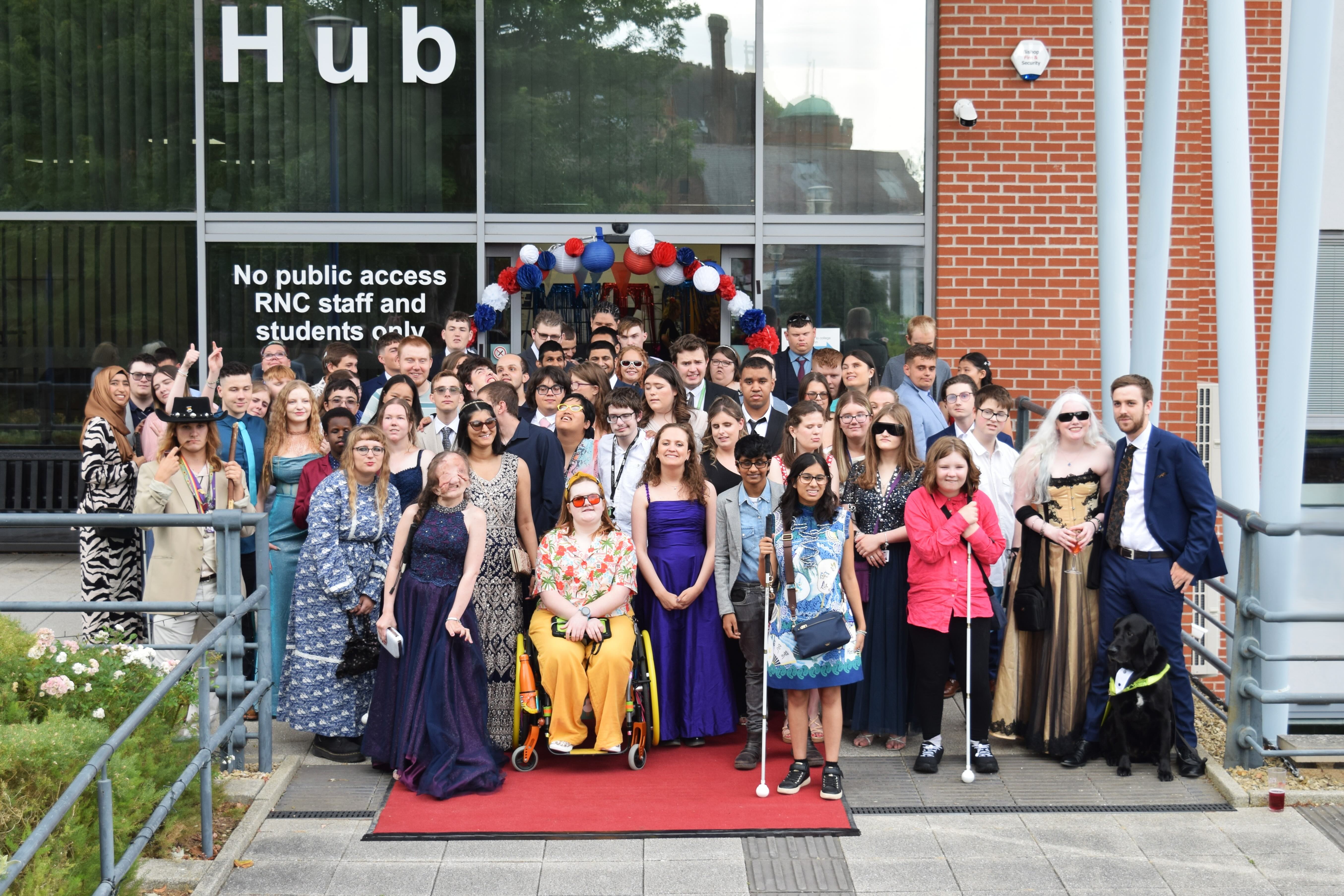 A large group of students stands in front of the College in evening wear on the eve of their prom