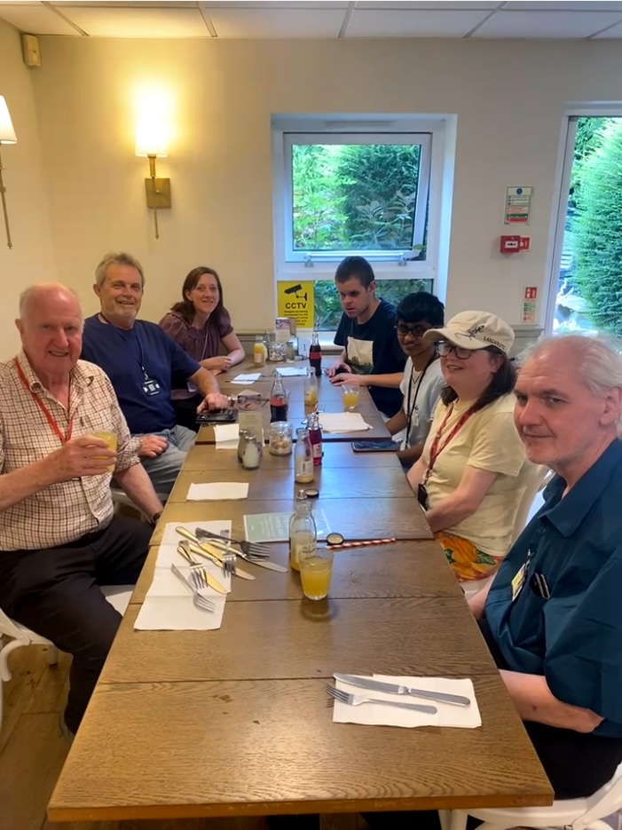 Sitting at the dinner table laid with cutlery, serviettes, condiments and drinks are Paul, Phil, Anika, Matteo, Sonali, Katie and Trefor