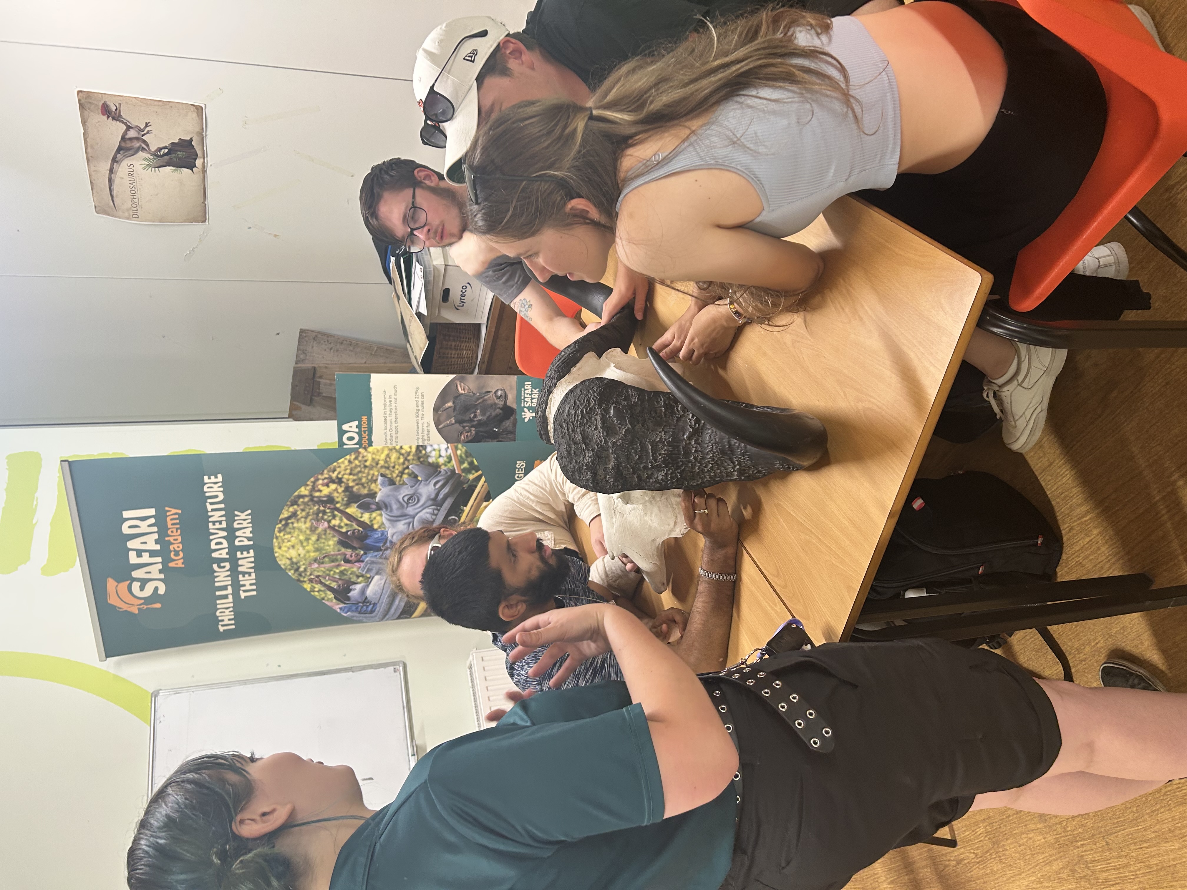 A group of students seated at a square table with a skull on the table and a person standing presenting