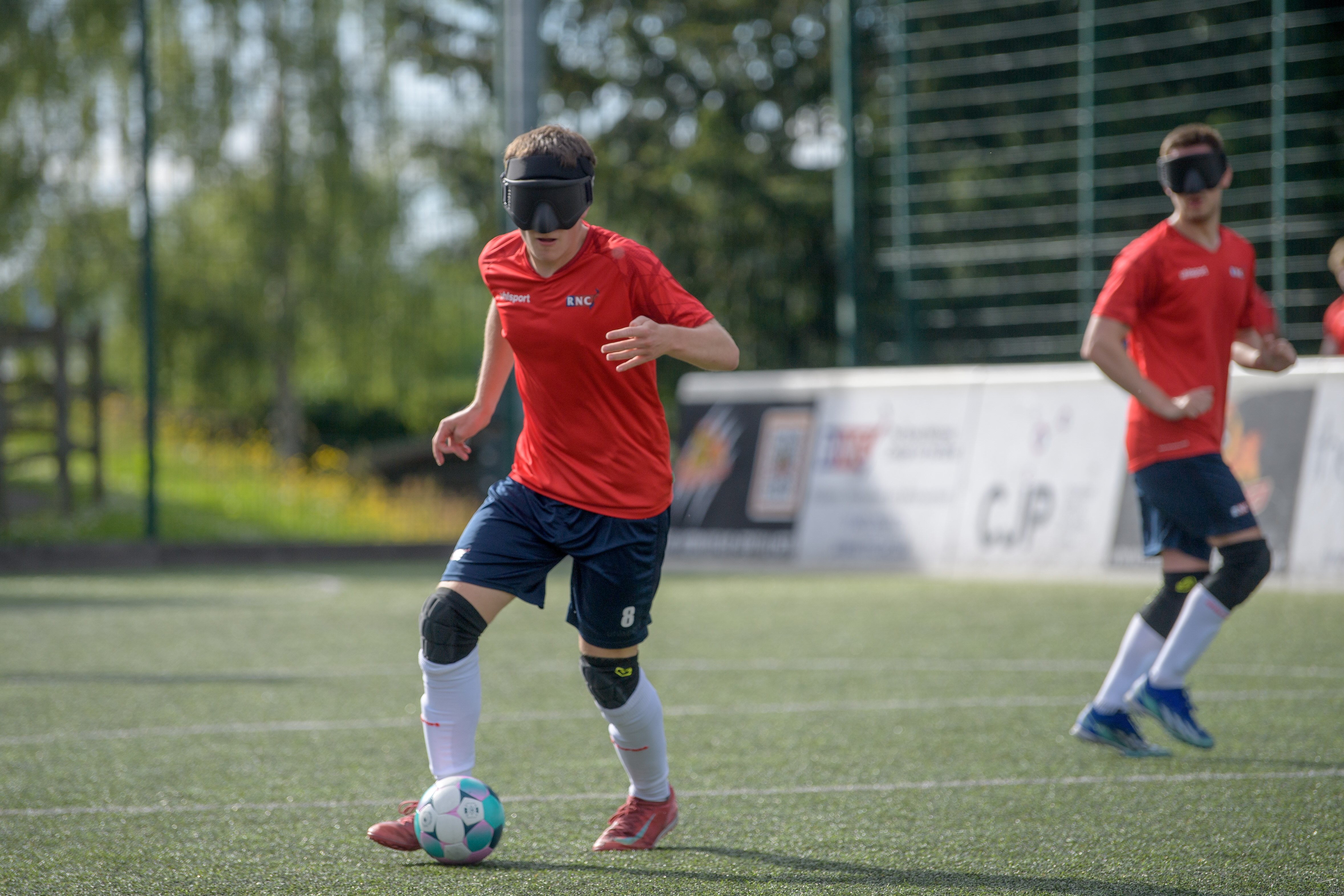 An RNC player on the ball wearing red shirt and navy shorts