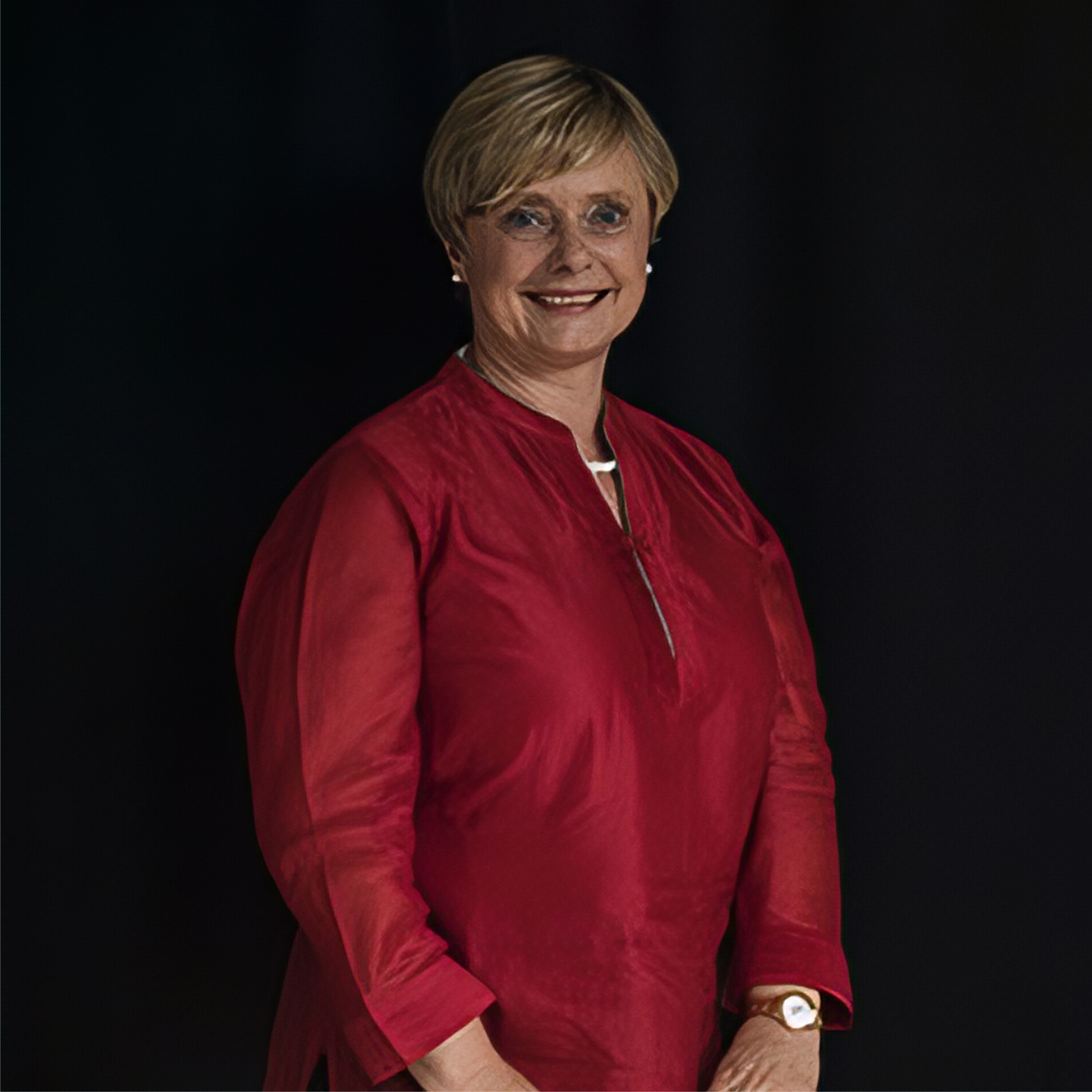 a portrait picture of a lady with short blonde hair smiling - she wears a satin red top