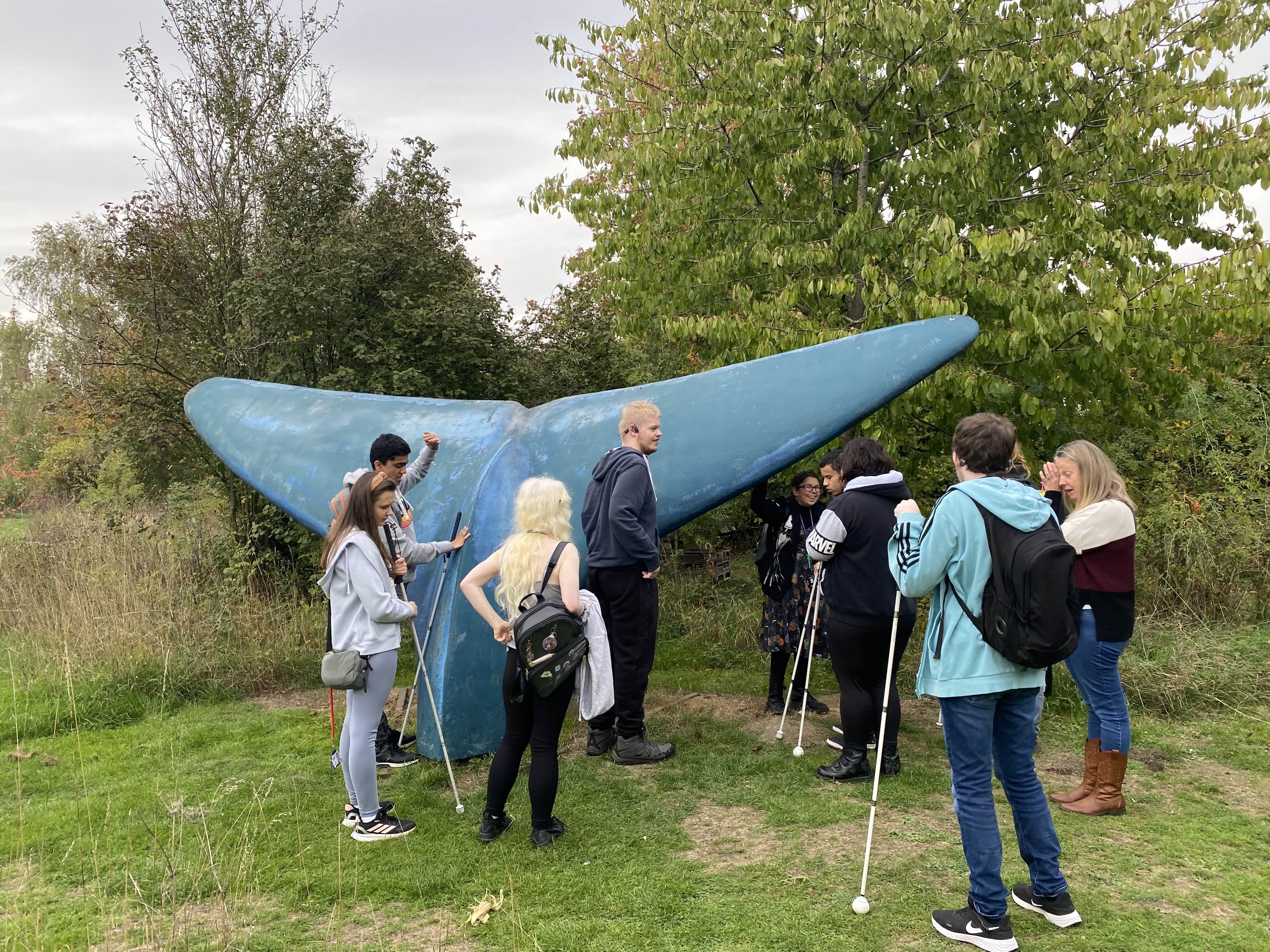 Students gather around a giant whale tail sculpture exploding from the grass