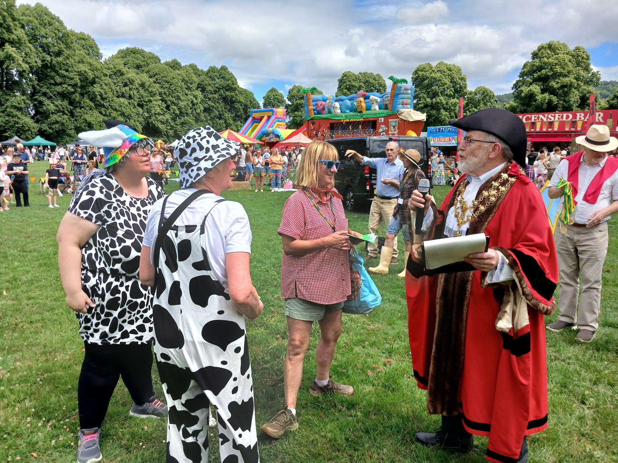 Mel and Mollie collect the prize from the Mayor who is wearing a red coat and tricorn hat. He's holding a clipboard and microphone